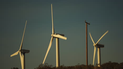 Steady-close-up-of-rotors-and-blades-of-3-wind-turbines-at-a-wind-farm-during-sunset-near-Palm-Springs-in-the-Mojave-Desert,-California,-USA