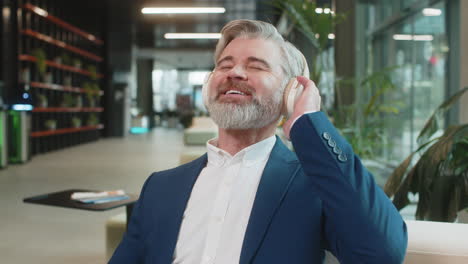 relaxed middleaged businessman in headphones listening music on smartphone in modern office lobby