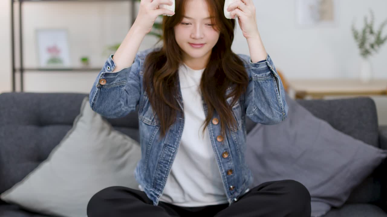 若い女性が白いヘッドホンを着け、目を閉じてソファで瞑想しています。