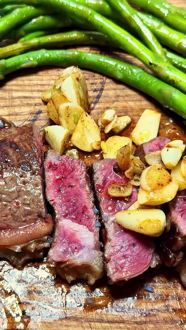 Cucchiaio che versa aglio arrostito su bistecca tagliata al sangue su tagliere di legno con fagiolini sullo sfondo, primo piano