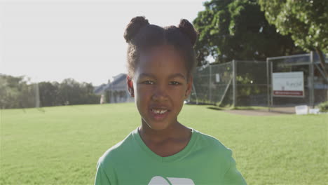 Biracial-girl-smiles-brightly-outdoors-wearing-a-green-recycling-t-shirt,-with-copy-space