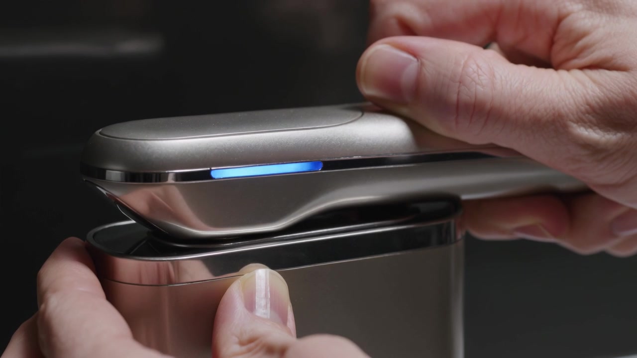 Entering hands placing metal handheld unit into docking base on dark bench, blue LED charging