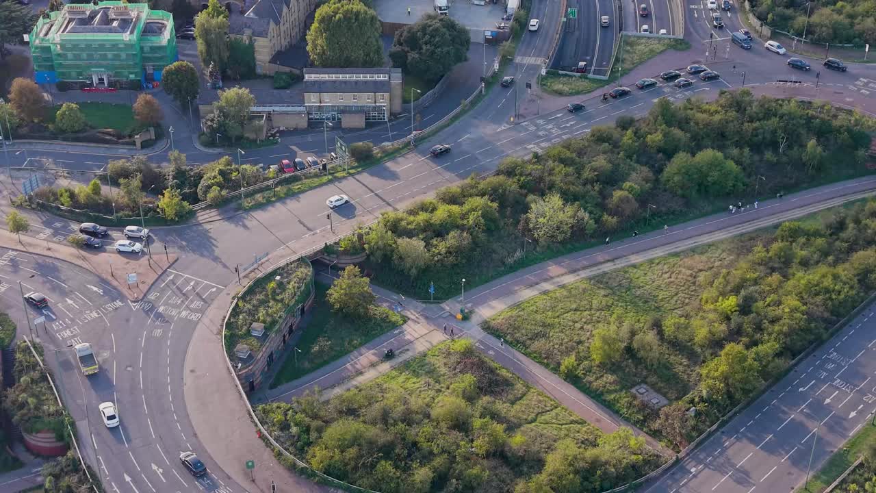 Aerial drone shot flying straight over the Green Man Roundabout, Leytonstone, East London. Camera shows the underpass, light traffic, and long shadows cast by the late afternoon September sun