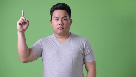 young handsome overweight asian man against green background