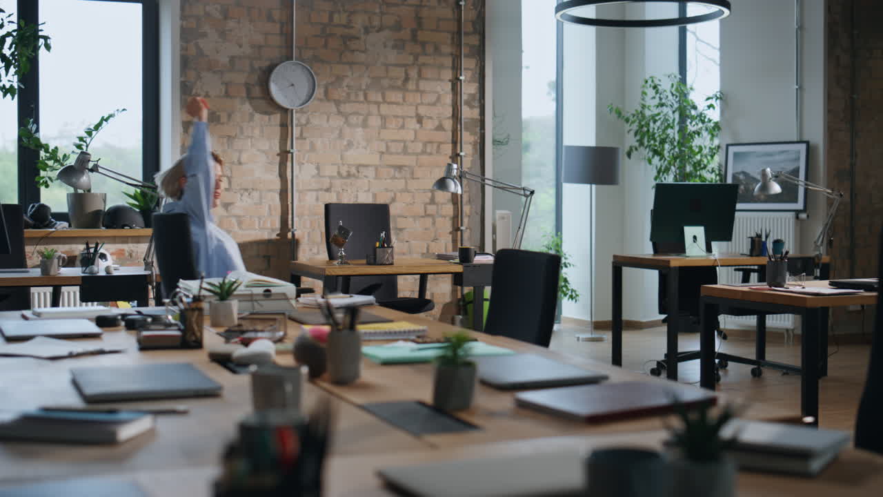Office worker riding chair between tables in empty office. Lady having fun alone