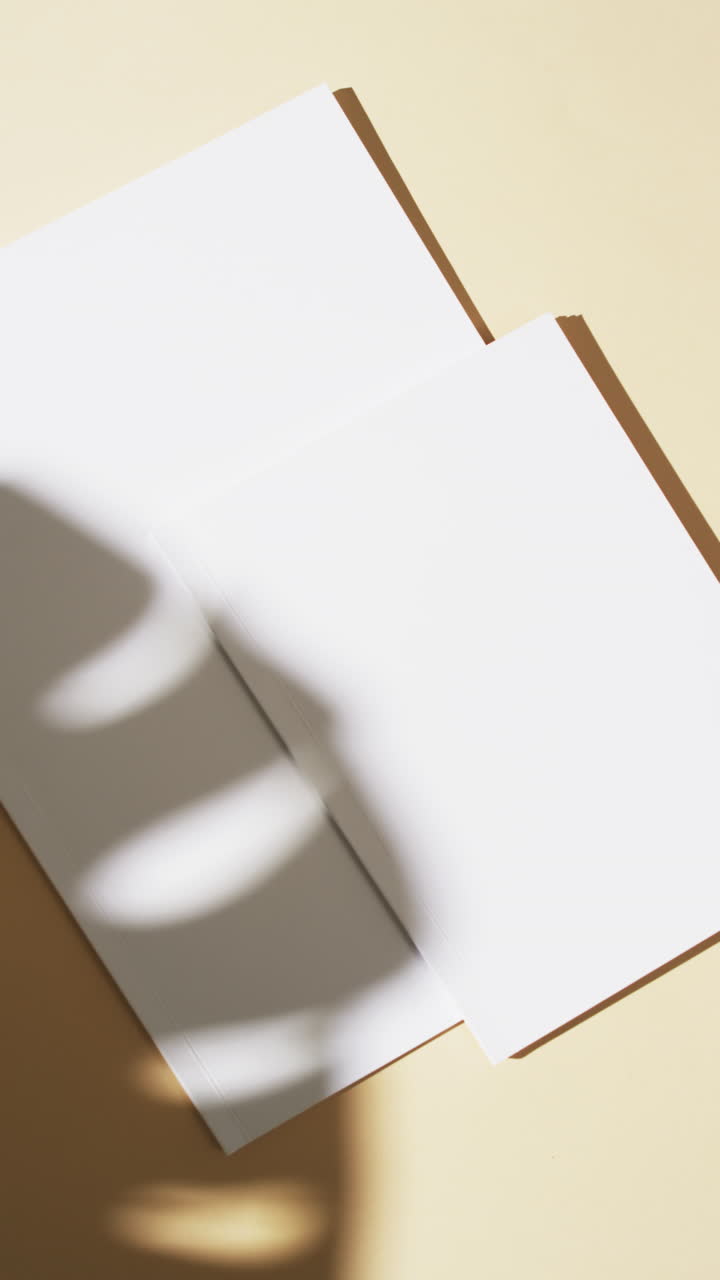 Vertical video of shadow of plant over books with blank pages and copy space on yellow background