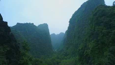 cinematic drone footage of majestic limestone peaks in misty and foggy weather. ricefields in wild jungle in the spring with boat tour canal in tam coc, ninh binh, vietnam