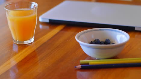 orange juice with laptop, blueberries and colored pencil on a table 4k