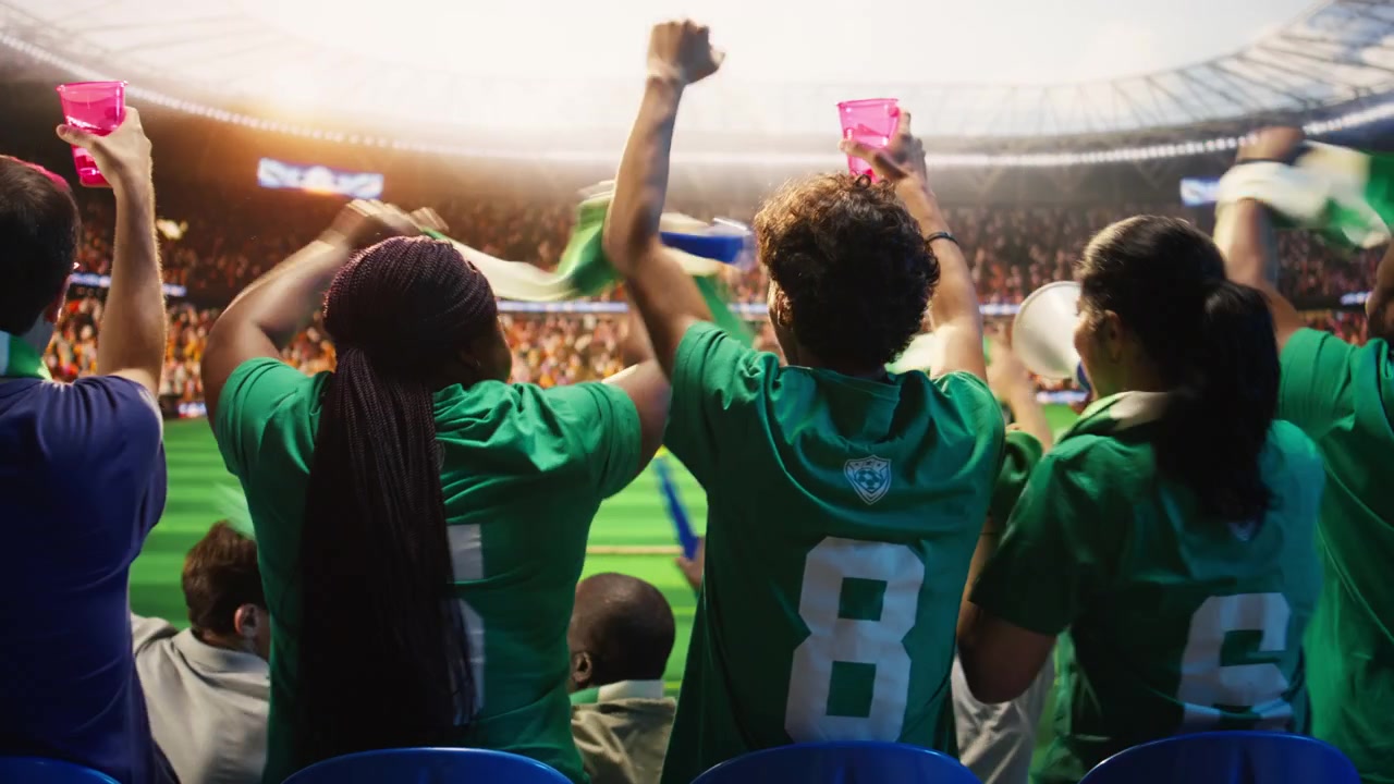 Vista trasera de aficionados al fútbol sosteniendo un vaso de bebida, agitando bufandas