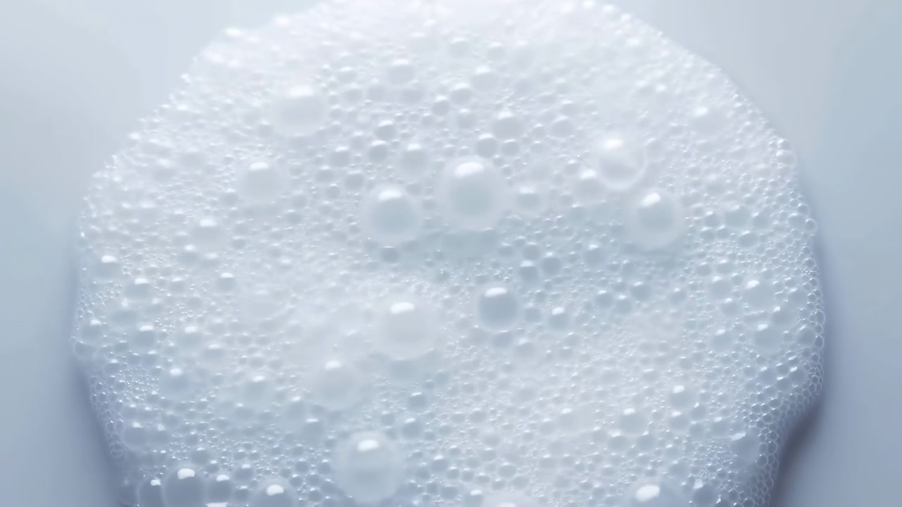 Spessa schiuma di sapone bianca si espande lentamente in grappoli arrotondati di microbolle e bolle più grandi, con riflessi lucidi e bagnati, contorni morbidi, riflessi luminosi e una texture pulita e igienica