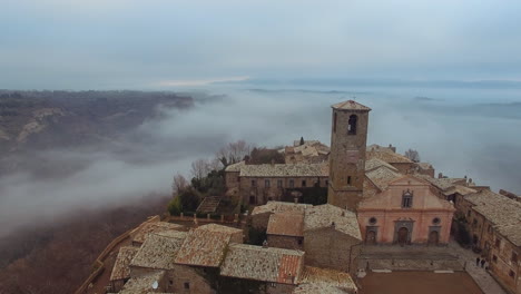 aerial dolly shot of civita di bagnoregio in the middle of the clouds at dusk. drone shot revealing the city and it's bridge passing thru the centre of the old city. 4k