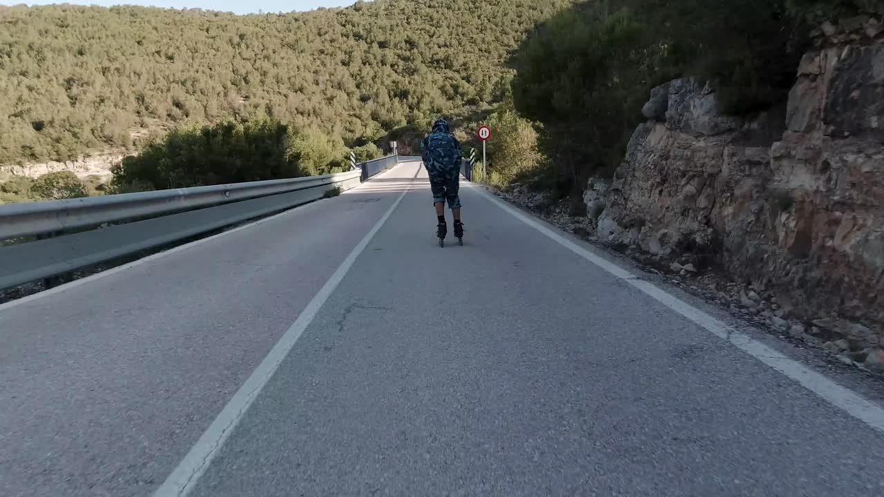 Follow shot of roller skater crossing bridge at sunset skating mountain road