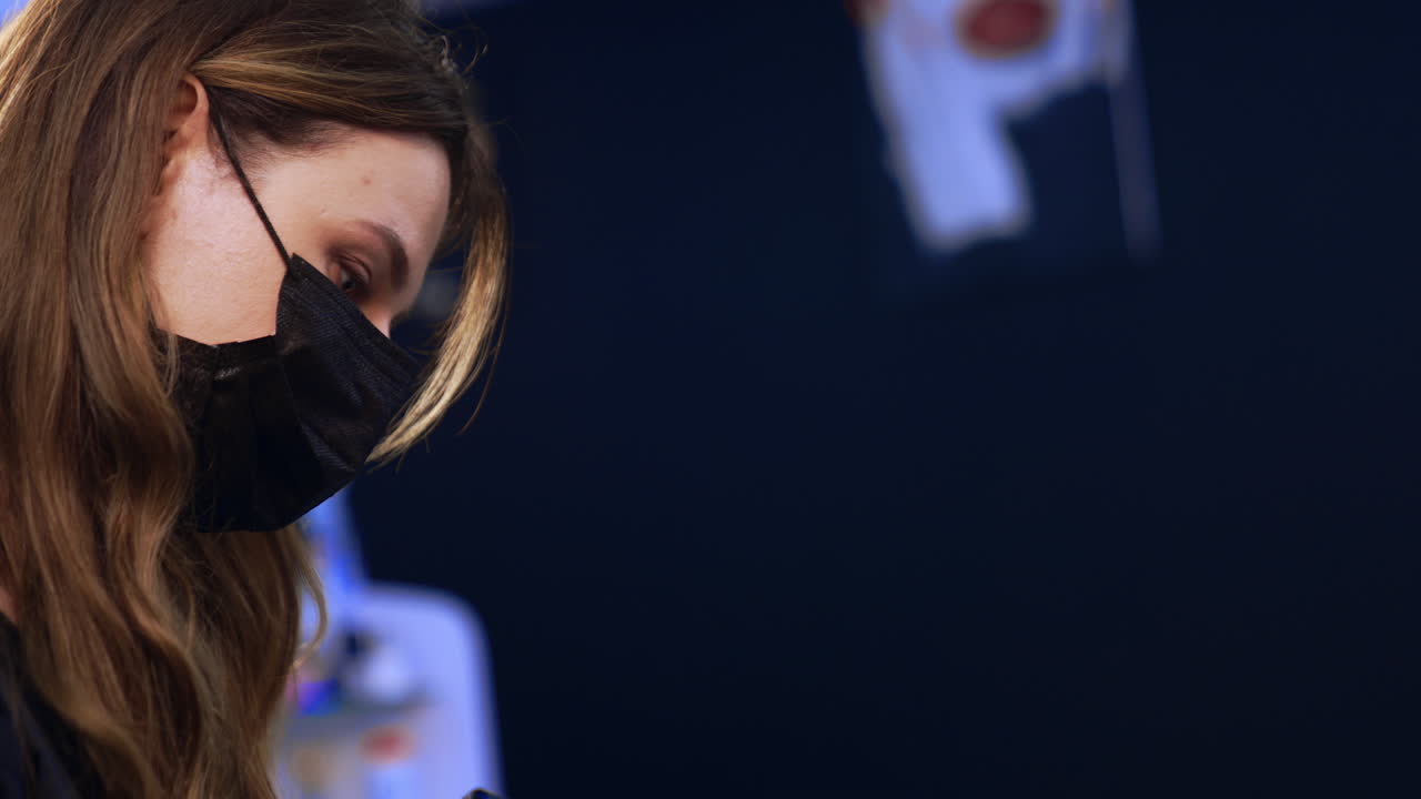 Beautician working in a modern beauty salon. Brunette brow master in mask performing the eyebrow make up. Side view.