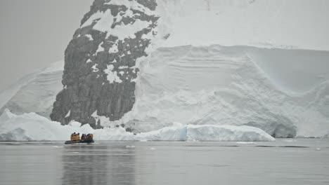 small zodiac boat in front of huge glacier and mountain coastline