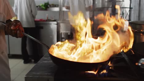 midsection of african american male chef frying vegetables in pan