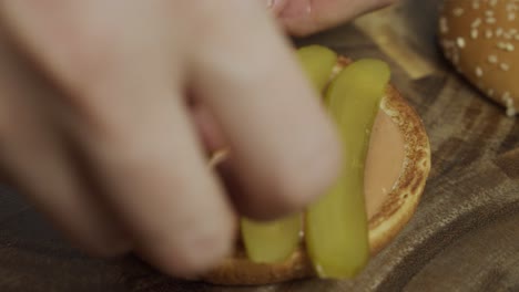 el chef pone pepinillos en capas encima del pan de hamburguesa