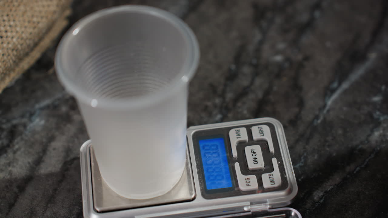 Close up of plastic cup placed on digital scale with woman resetting weight as soft shadow casts across marble countertop, showcasing kitchen preparation, precision measurement