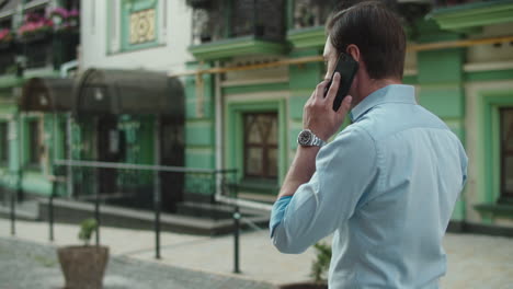 Back-view-of-businessman-walking-with-mobile-phone-at-city-street