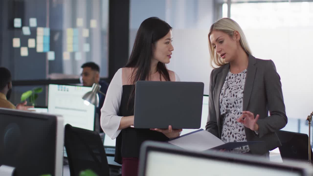 dos mujeres de negocios diversas discutiendo juntas y usando una computadora portátil en la mesa