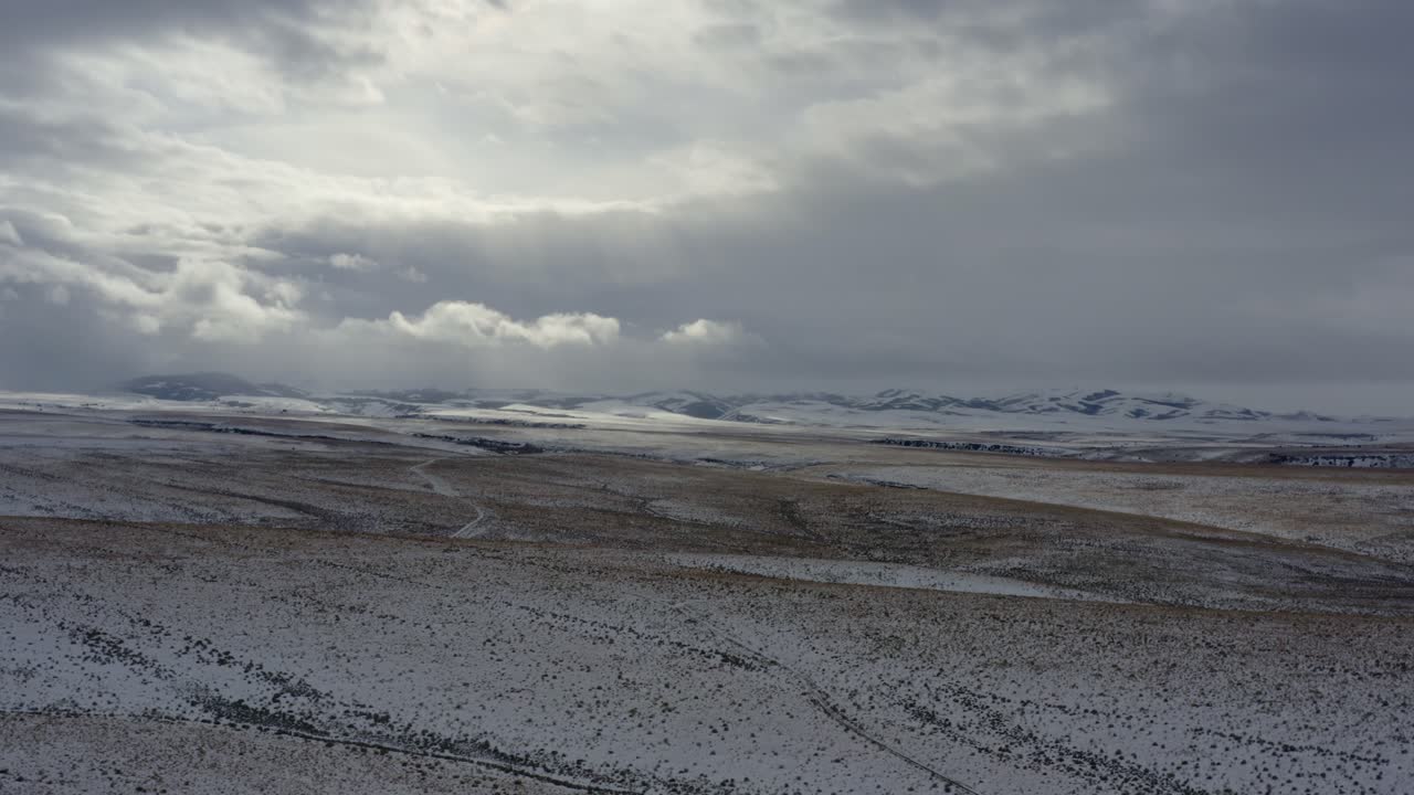 Expansive vista plain with snowy mountains in the distance, sun shining through clouds