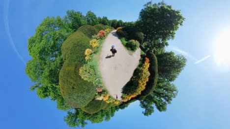 360-degree “tiny planet” projection of a garden path bordered by colorful flowers and shaped hedges. shot in a botanical garden