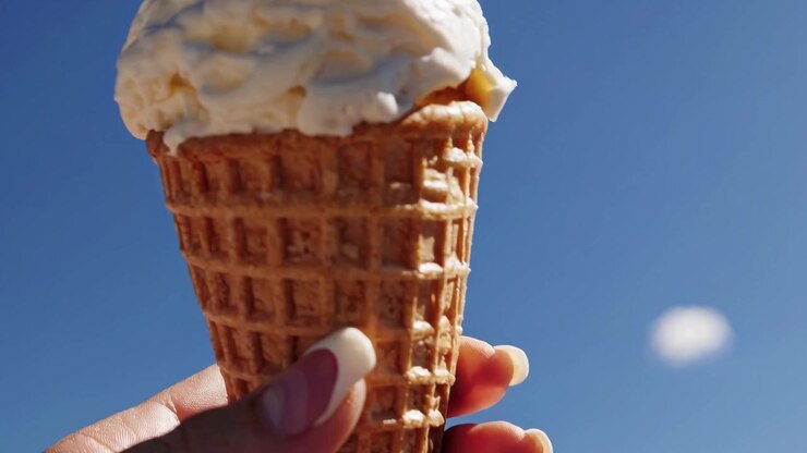 Primo piano di gelato che si scioglie in un cono waffle contro il cielo blu