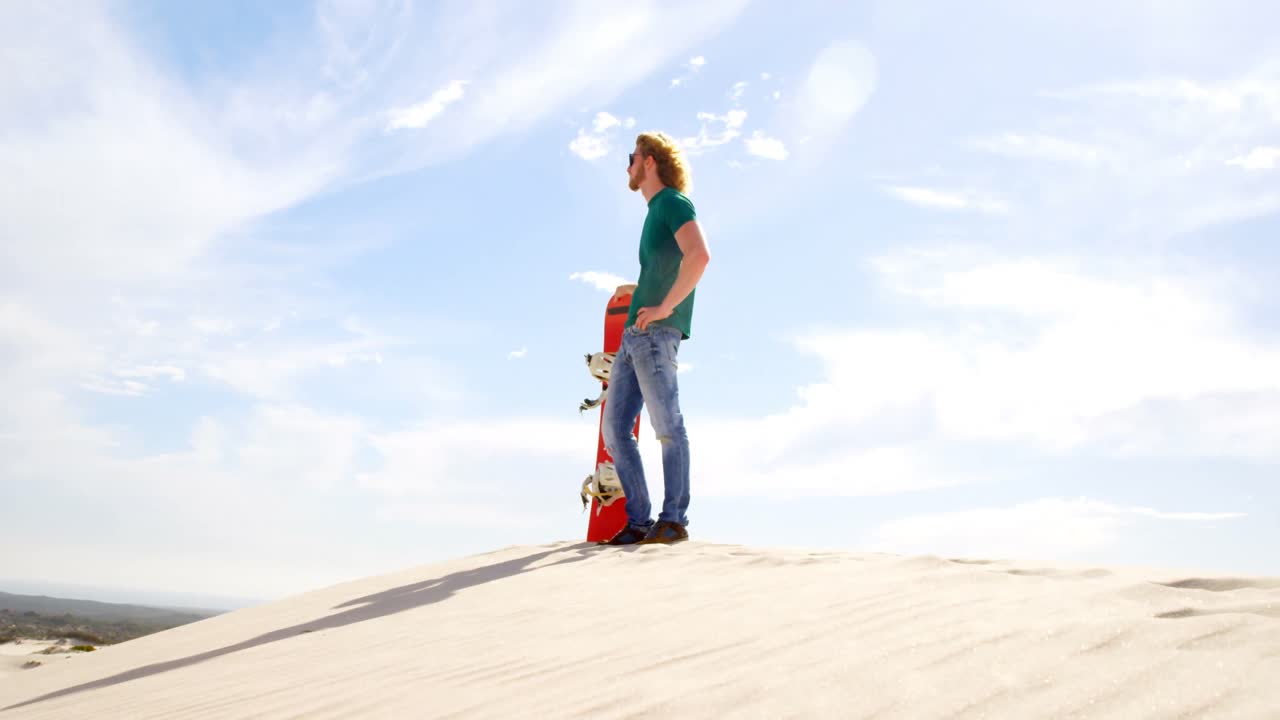 Uomo con tavola da sandboarding che guarda in lontananza nel deserto 4k