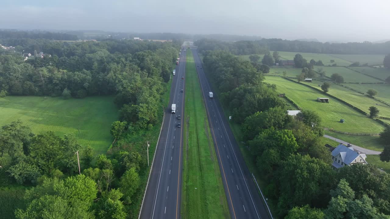 Traffic on expressway interstate in America Suburb. Aerial rising wide shot. Sunny day in summer. Farm fields and houses in suburbia of Pennsylvania