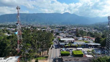 Cars-on-main-road-of-Caribbean-town-with-transmission-tower-and-park-trees