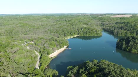 Inclinación-Aérea-Hacia-Abajo-De-Una-Pequeña-Playa-De-Montaña-En-Un-Hermoso-Lago-Natural-Verde-Durante-Una-Calurosa-Y-Brillante-Tarde-De-Verano