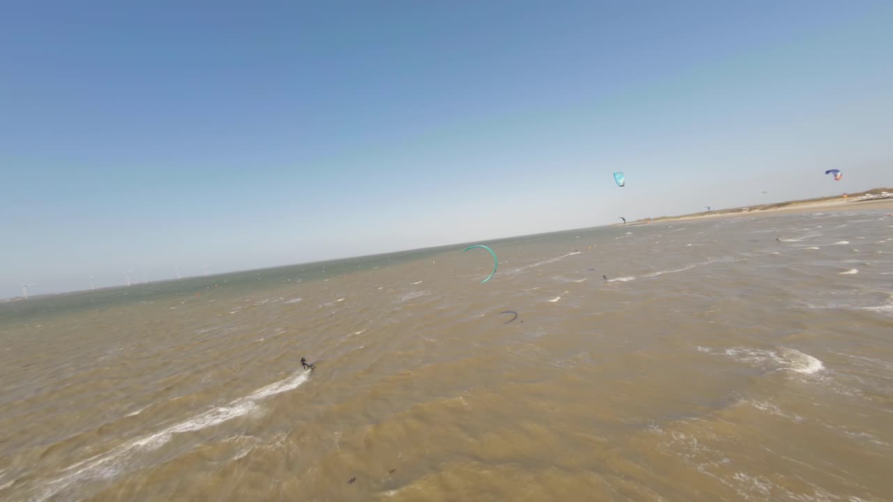 Aerial tracking shot of kite surfers riding murky waves near Roompot beach