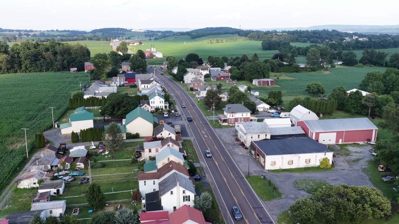 Tofelts vei går gjennom en liten jordbruksby med hvite hus og røde låver, biler kjører forbi kornåkre og bølgende åser nær Maxatawny, Pennsylvania. Vidvinkel droneopptak