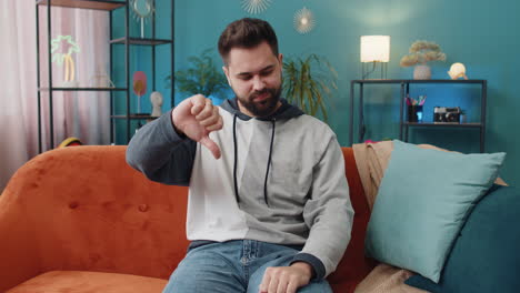 upset caucasian man showing thumbs down dislike bad work disapproval dissatisfied feedback at home