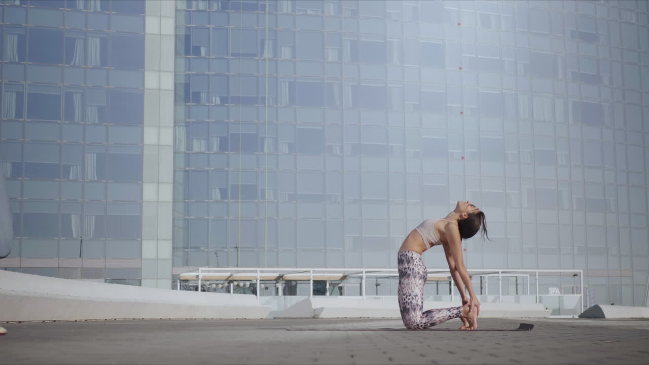 거리에서 매트에 낙타 포즈를 취하는 여자. 도시 거리에서 몸을  ⁇ 는 소녀