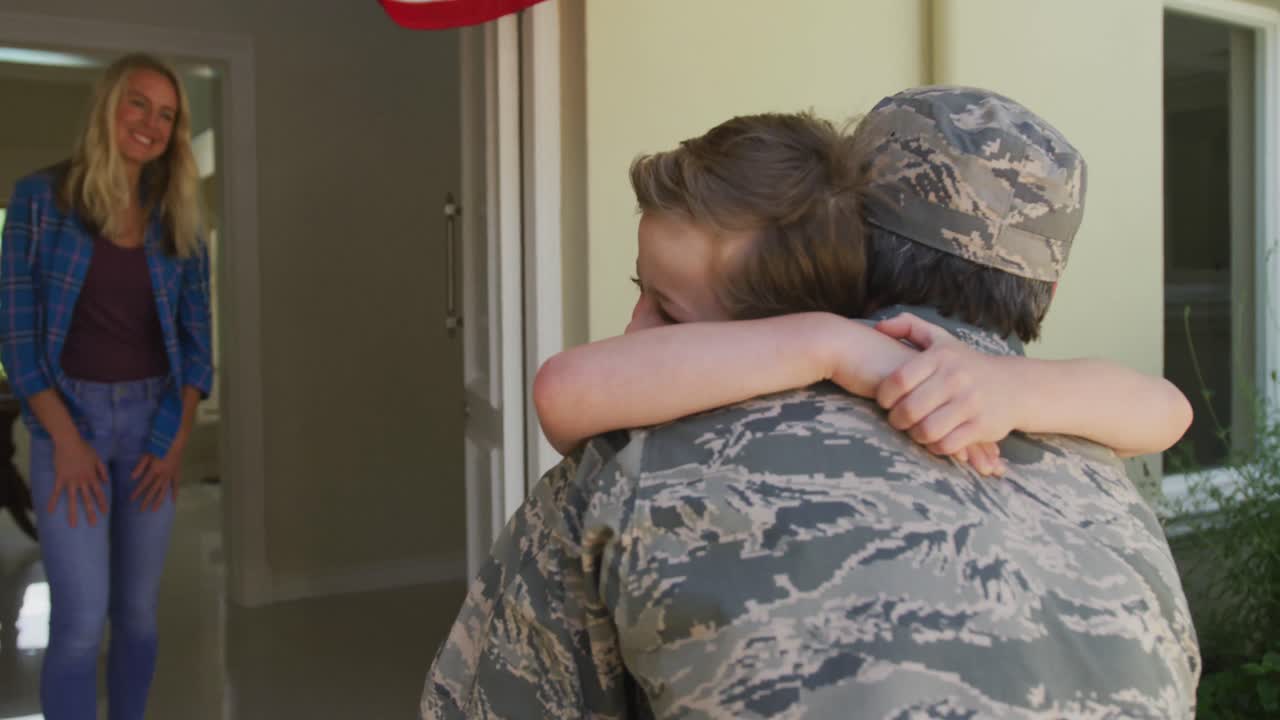 백인 남성 군인이 웃는 아들을 아내와 미국  ⁇ 발 위에 안아주고 있습니다.