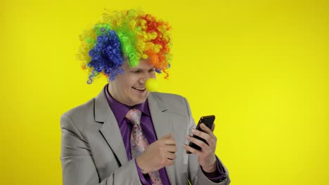 Clown-businessman-entrepreneur-in-wig-using-app-on-smartphone-for-online-work