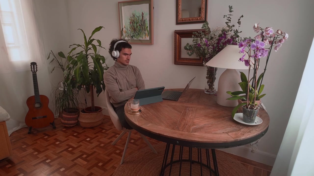 Timelapse of a man working on a laptop at home while using a phone and playing guitar.