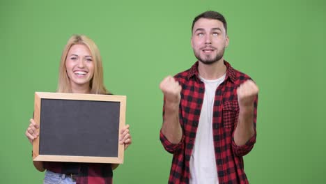 young couple holding blackboard and looking excited together