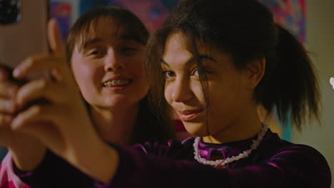 two friends take a selfie using phone they smile and pose african american and asian girls sit together in cozy room and take a selfie using phone they smile and pose two multi ethnic friends have fun and spend leisure time at home friends relationship