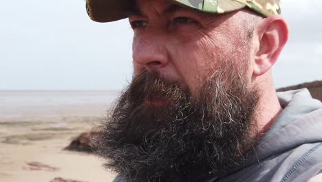 bearded urban man wearing baseball cap with mental health frustration looking across windy beach