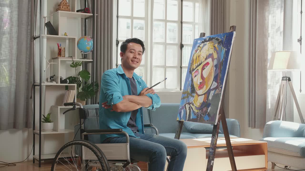 Hind View An Asian Artist Man In Wheelchair Holding Paintbrush Mixed Colour Turn To Cross His Arms And Smile While Painting A Girl On The Canvas