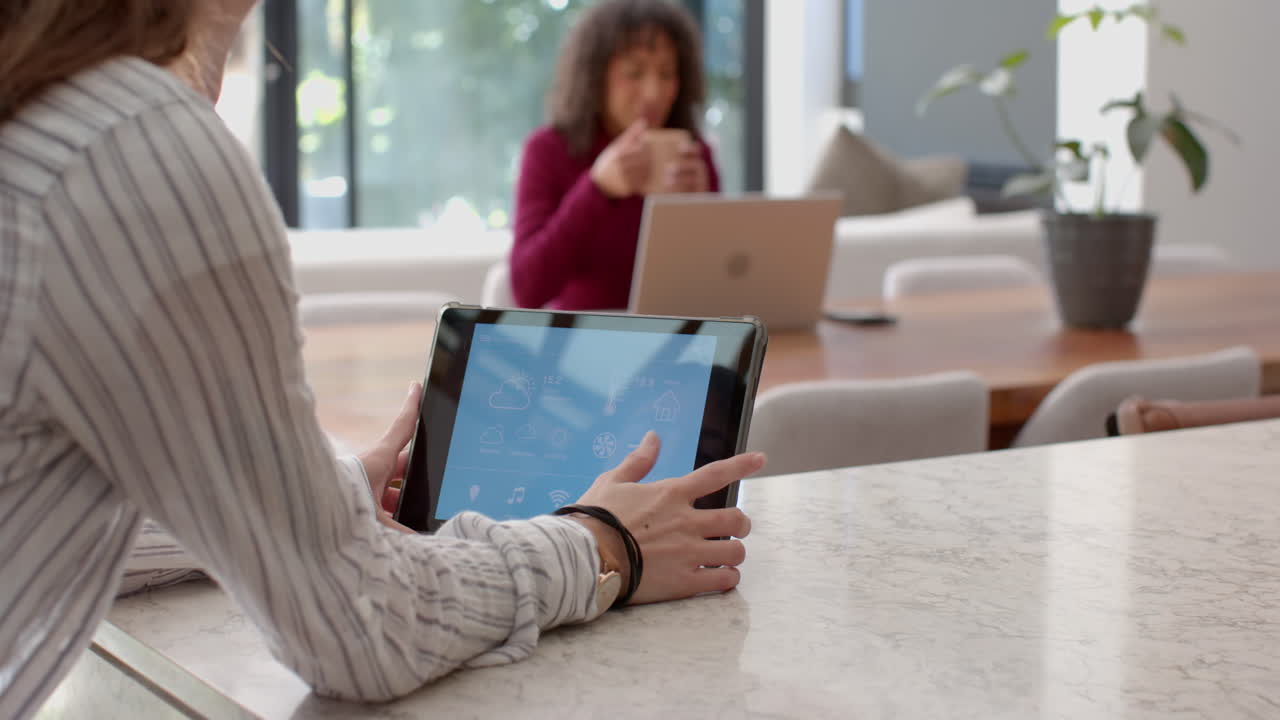 Using tablet for home automation, woman in background working on laptop