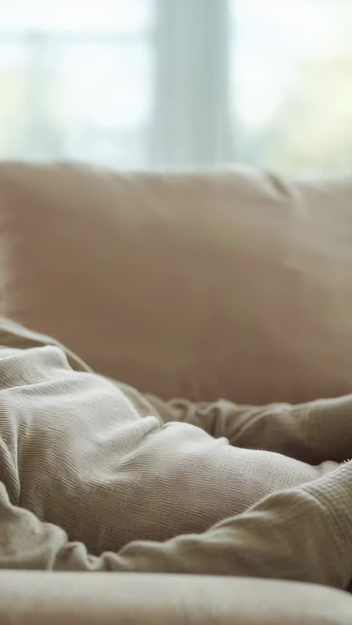 Video verticale: si sente una voiceover fuori campo, uomo con maglia color sabbia seduto sul divano che si sposta e sorride, spazio per il testo