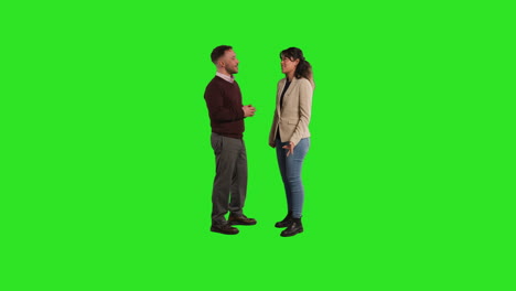 full length studio portrait of male and female teachers or businesspeople talking and looking at camera against green screen