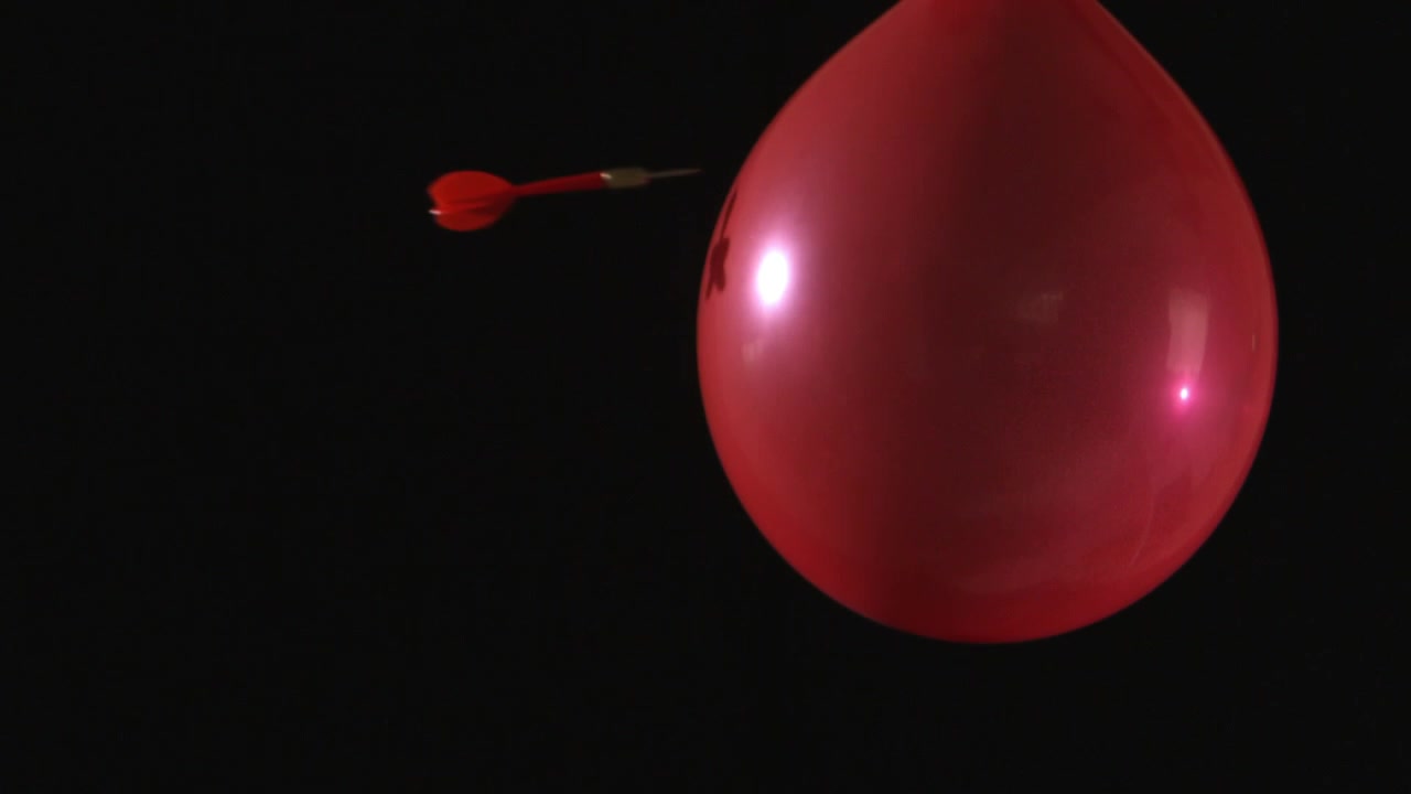 Fléchette perçant un ballon rouge au ralenti
