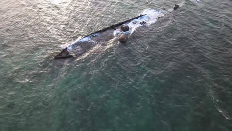 drone aerial flying low over a shipwreck in the ocean with waves crashing into it