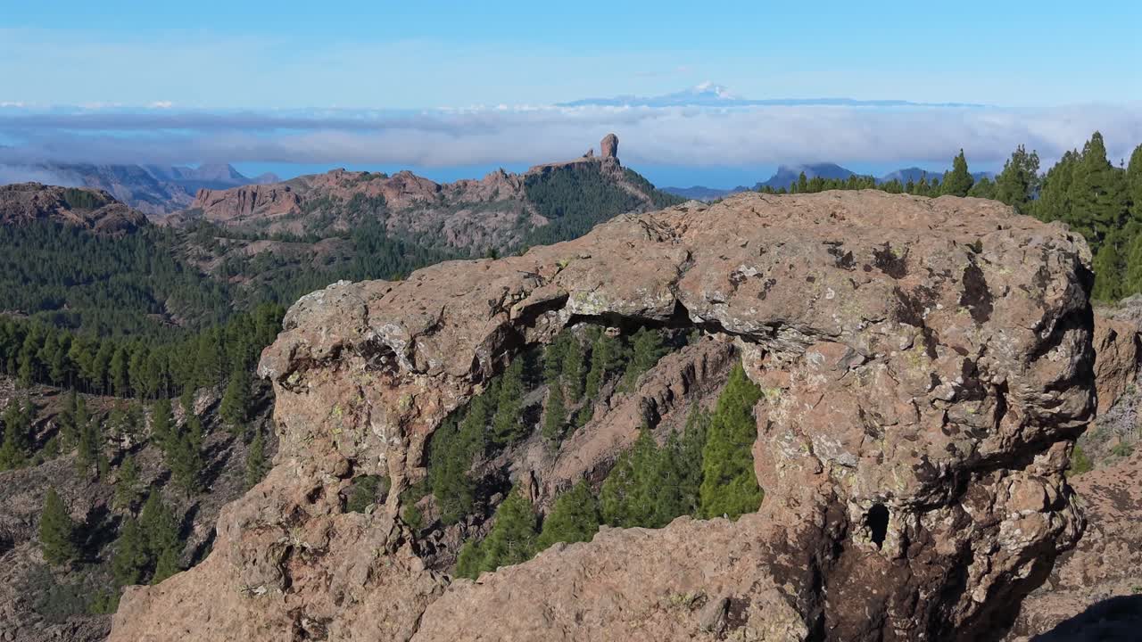 Splendida ripresa aerea che rivela lentamente il monolito Roque Nublo e il vulcano Teide attraverso un arco di roccia naturale a Gran Canaria (Gañifa)