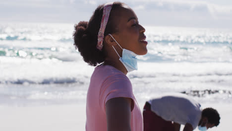 african american couple with face masks collecting rubbish from the beach