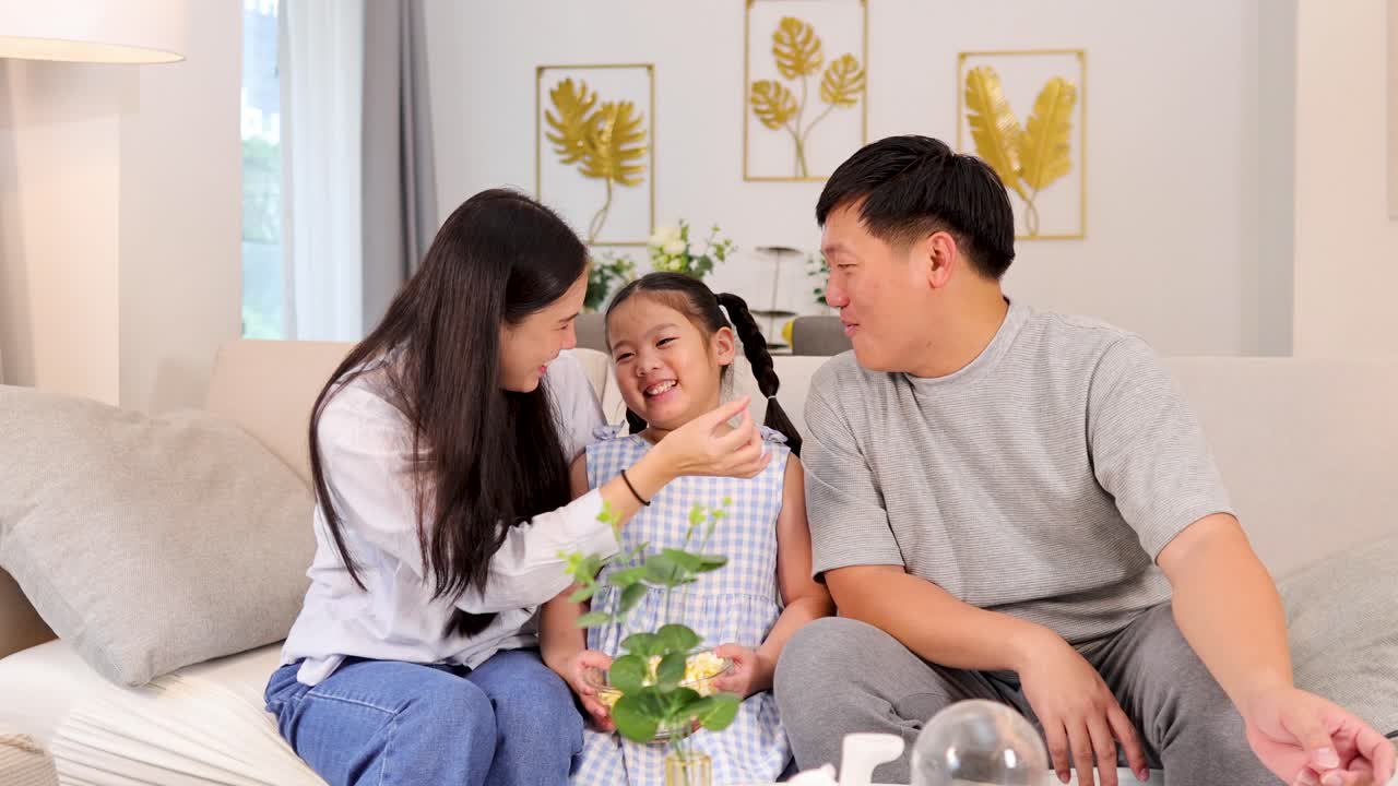 A family enjoys quality time together on a couch, sharing laughter and popcorn in a cozy living room setting