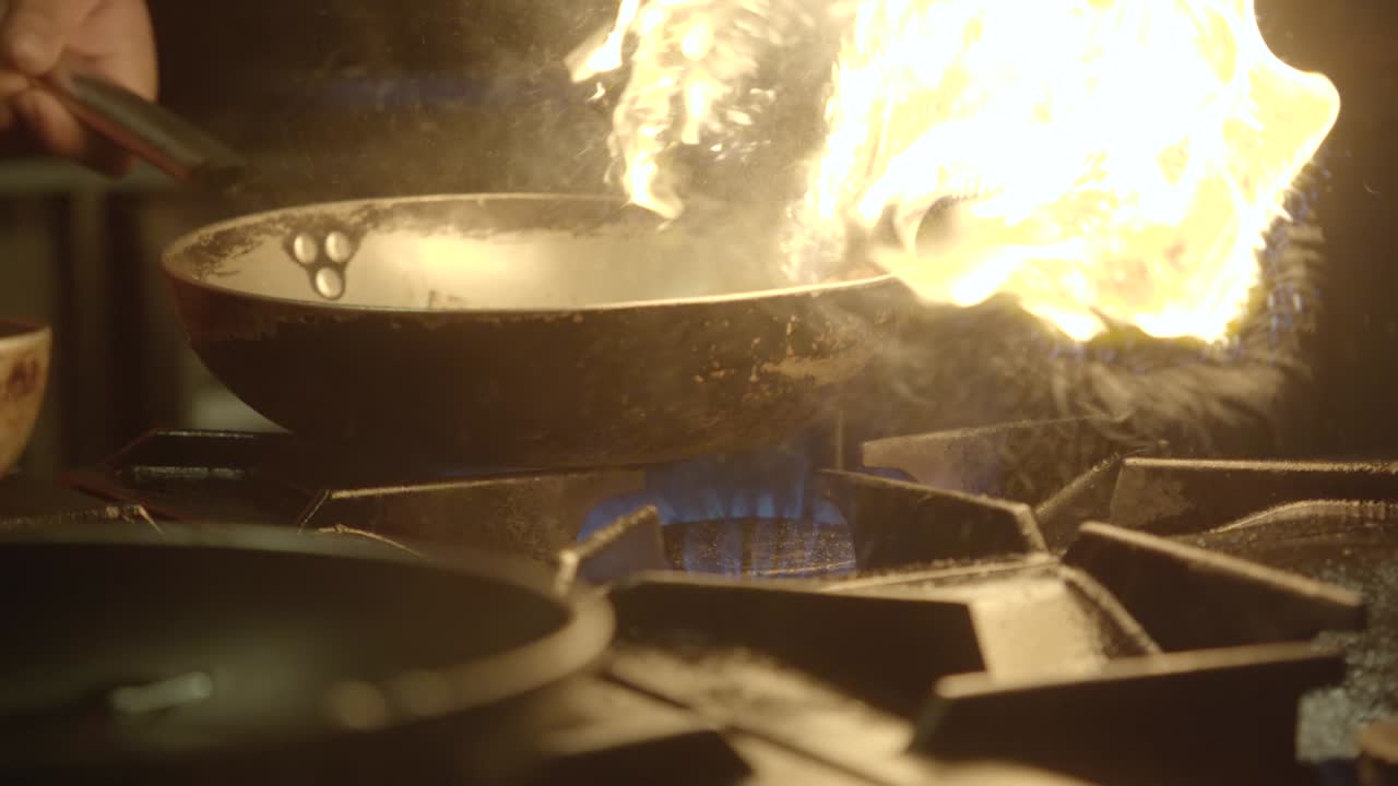 Motion shot chef holds frying pan on fire, kitchen concept Slow motion